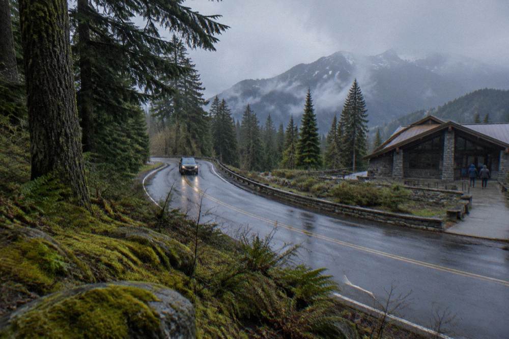 A paved mountain road winding upward through forest toward distant mountain peaks