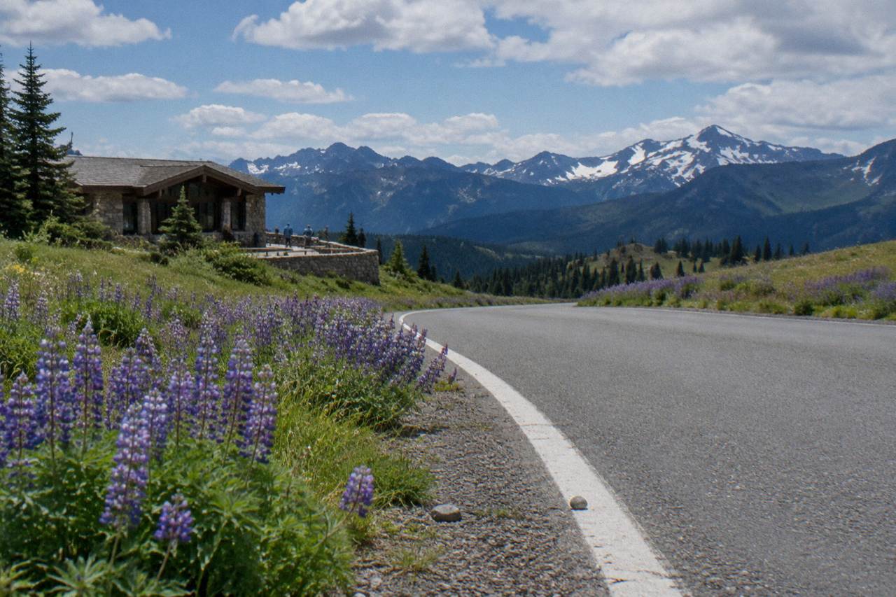 A paved mountain road curving toward open ridgeline meadows under scattered clouds