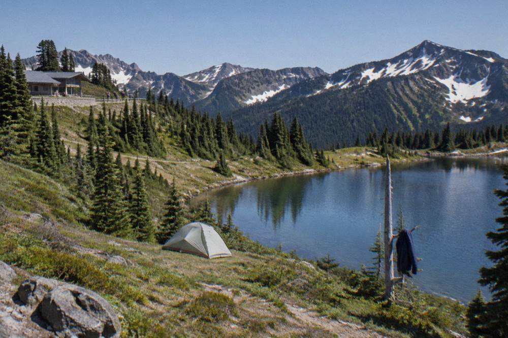 A backpacker's tent beside an alpine lake ringed by forested ridges