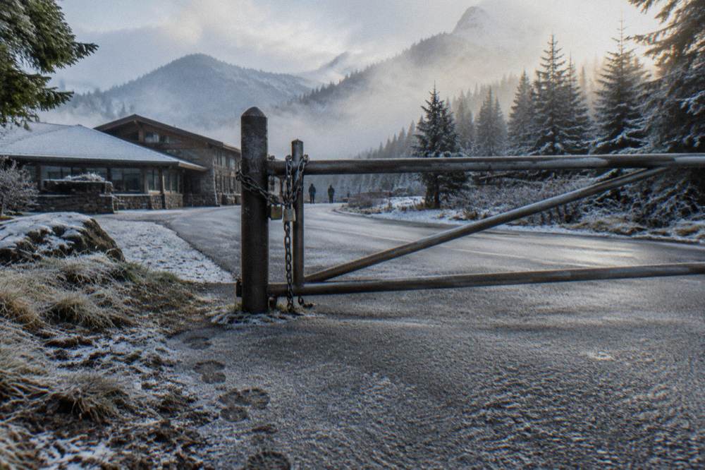 A closed metal gate across a forest road with mist in the trees.