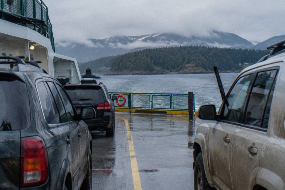 A ferry deck with vehicles parked and forested hills across the water