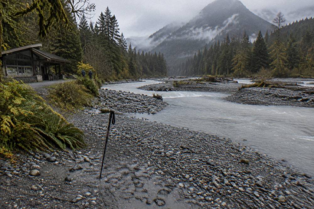 A wide glacial river running gray between forested valley walls