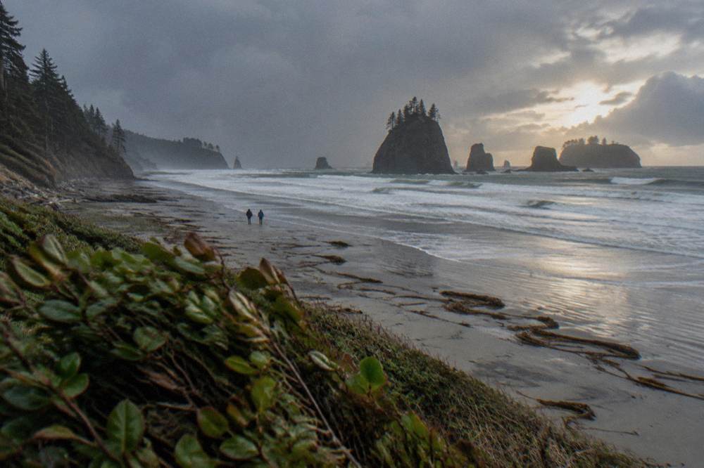 Waves breaking on a wide sandy beach with sea stacks offshore in late light