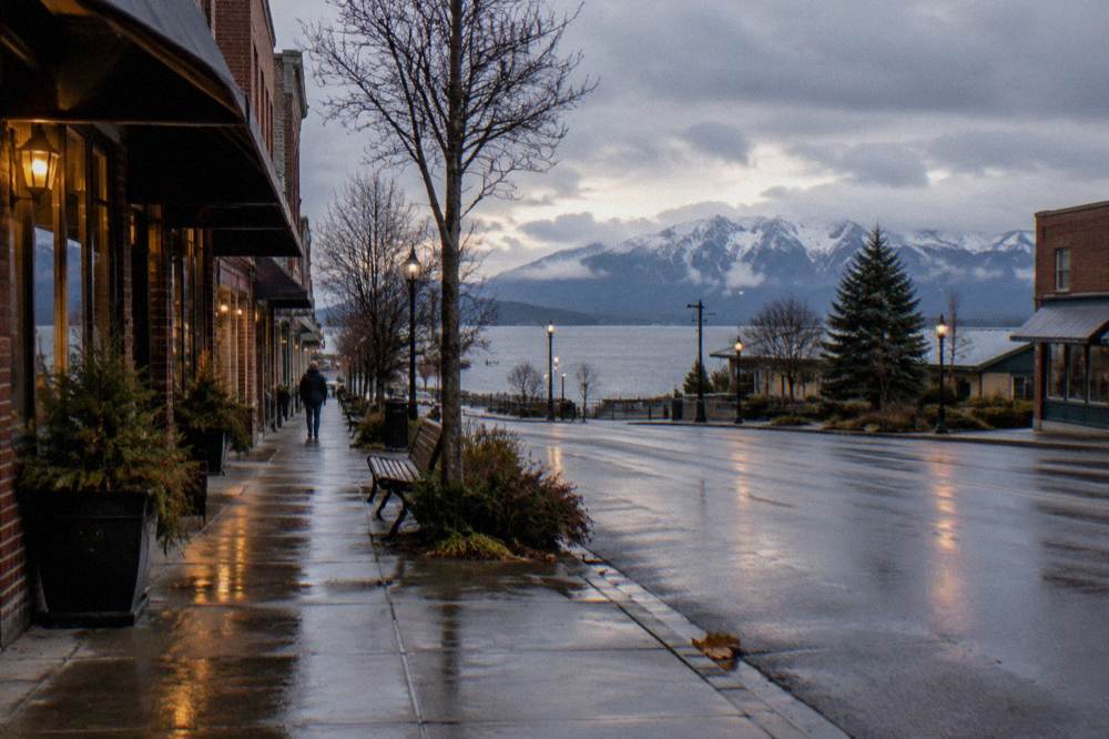 Quiet small-town street with storefronts and distant mountains under a partly cloudy sky