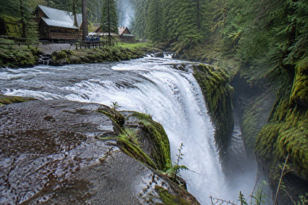 A wide waterfall pouring over a mossy rock ledge into a narrow forest gorge