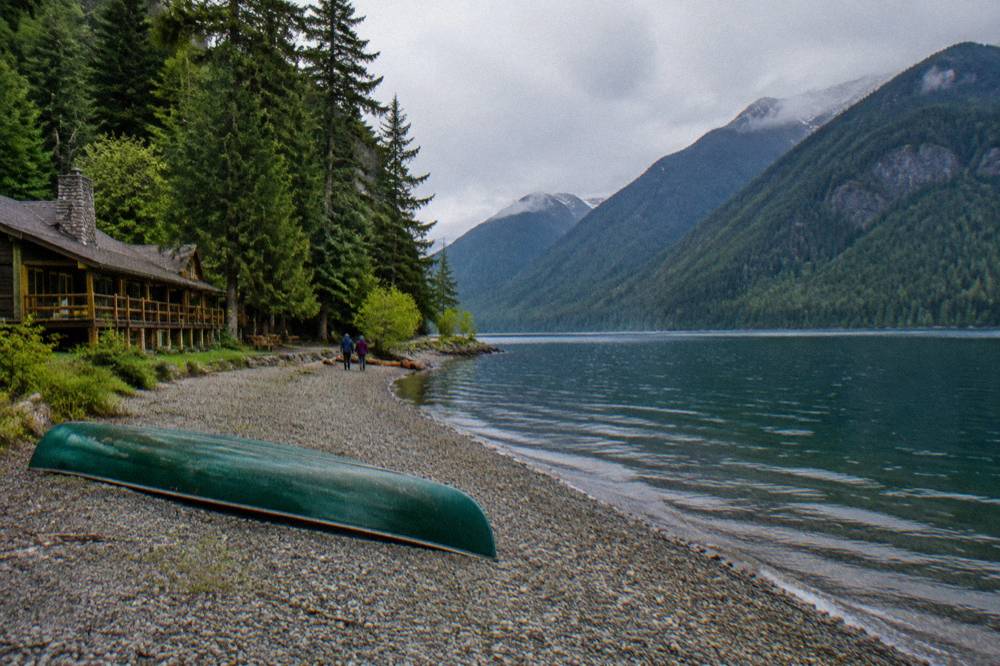 A van parked at a mountain overlook with forested slopes descending toward a glacial lake