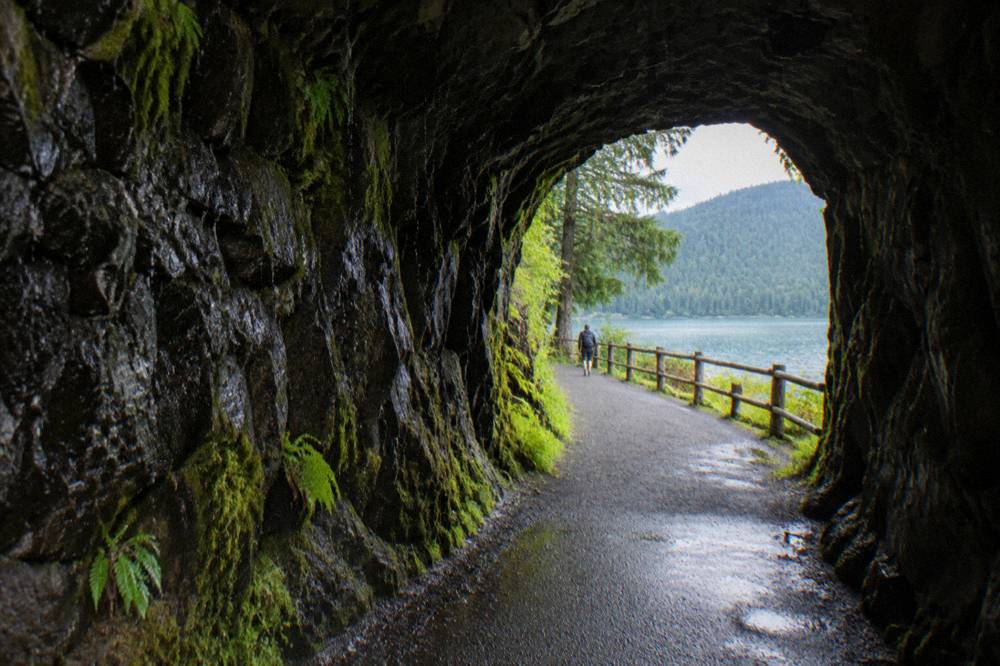 A paved trail passing through a rock tunnel beside a lake
