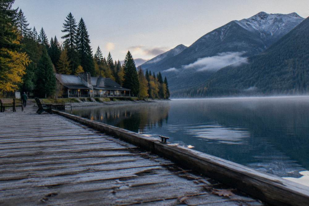 A wooden dock extending into a still blue lake with mountains beyond