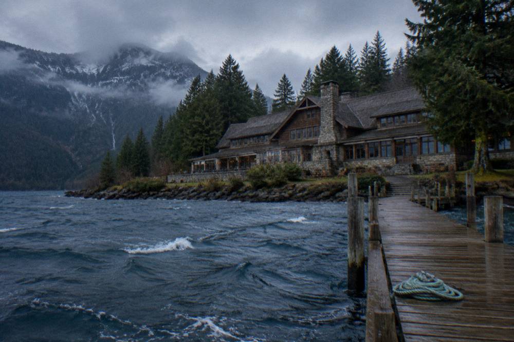 A historic lakeside lodge with a long wooden dock and mountains behind