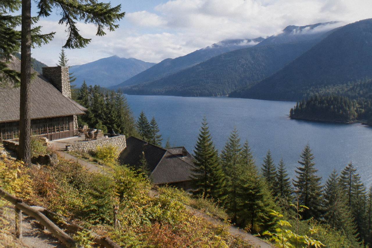 A deep blue glacial lake ringed by forested mountains under scattered clouds
