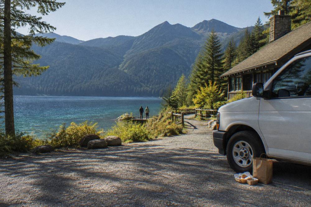 Tour van parked at a scenic overlook above a glacial lake and forested ridges