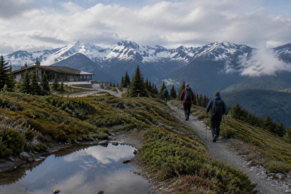 A group of hikers with trekking poles walking a mountain ridge trail under clearing skies