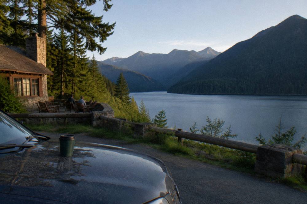 Car parked at a scenic overlook above a deep blue lake ringed by forested mountains