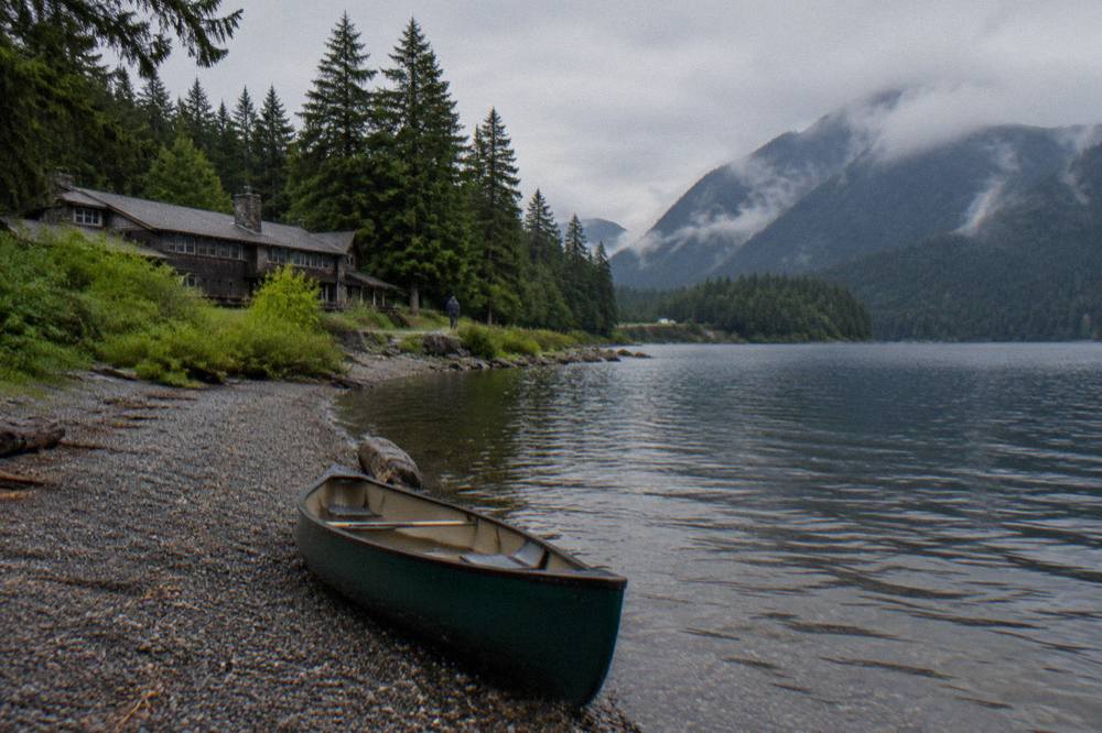 A van parked at a gravel pullout beside a forested lake shoreline under overcast sky