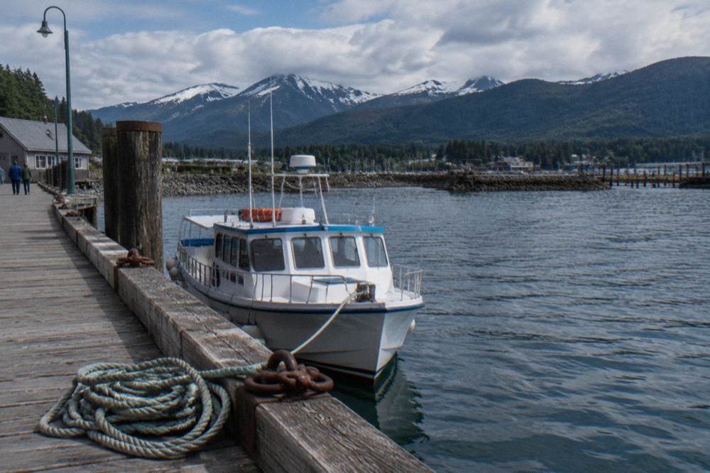 A small passenger boat at a wooden wharf with forested hills behind
